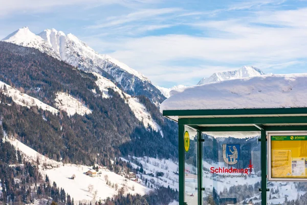 Fermata autobus austriaca, cartello comprensorio sciistico Schladming-Dachstein, Intorno alla strada innevata, alberi e montagne . — Foto Stock