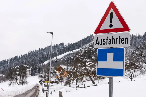 Segnale di avvertimento stradale a triangolo rosso - Altro pericolo con testo Ausfahrten che significa uscite. Strada innevata, alberi e montagne. Austria — Foto Stock