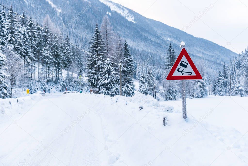 Black ice danger - traffic sign, warning, winter services, Schladming Dachstein. Snow covered road and trees. Austria, Europa