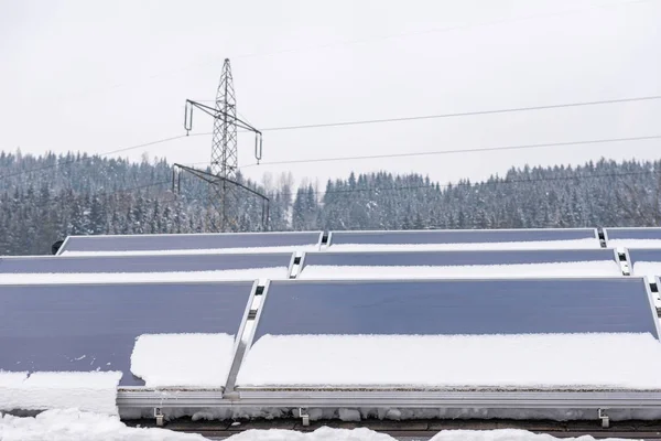 Fotovoltaik paneller kısmen karla kaplı, evin çatısına yerleştirilmiş. Arka planda elektrik şebekesinin bir elementi var. Kabloların üzerinde yüksek voltajlı bir elektrik direği..