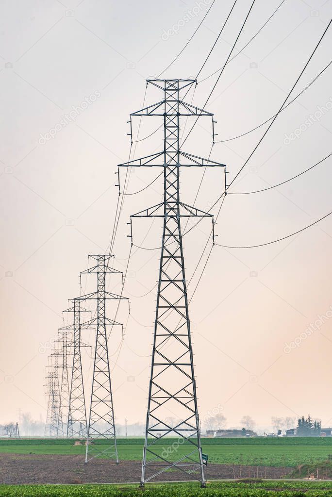 Electricity distribution system. High voltage overhead power line, power pylon, steel lattice tower standing in the green field.