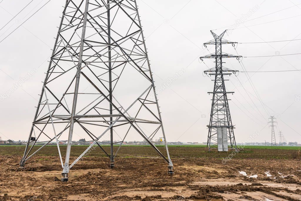 Electricity distribution system. High voltage overhead power line, power pylon, steel lattice tower standing in the green field.