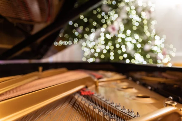 Ön planda görünür telleri olan altın piyano iç tasarımı. Arka planda süslerle süslenmiş bulanık bir Noel ağacı ve Noel ağacı ışıkları. Büyük bokeh ve bölgesel odak.