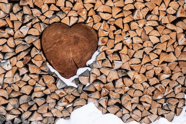 Valentines Day background. Wood for the fireplace arranged in an artistic way with a wooden heart in the middle. Winter scenery with snow around. Natural, wooden background.