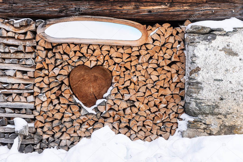 Wood for the fireplace arranged in an artistic way with a wooden heart in the middle. Winter scenery with snow around. Valentines Day background. 