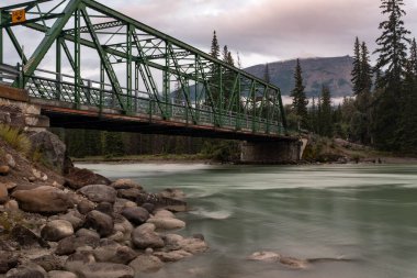 Jasper Ulusal Parkı 'ndaki Athabasca Nehri üzerinde yeşil bir demir köprü, uzun süre maruz kaldıkları için sular pürüzsüzdür.