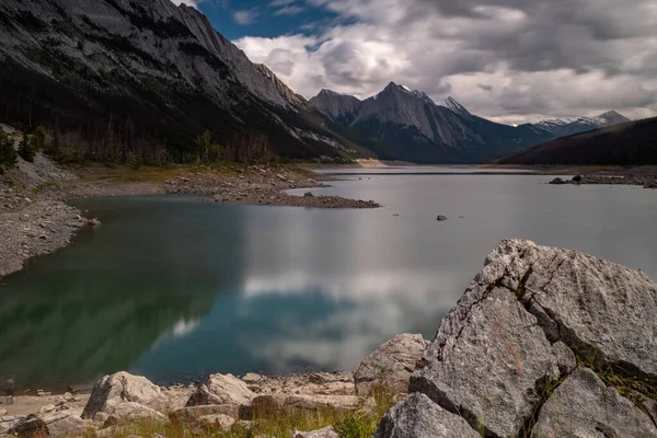 Una toma de la exposición larga del lago de la medicina, el parque nacional de Jasper, de la cabeza del lago, las aguas del lago son lisas debido a la exposición larga. Con rocas en primer plano . — Foto de Stock