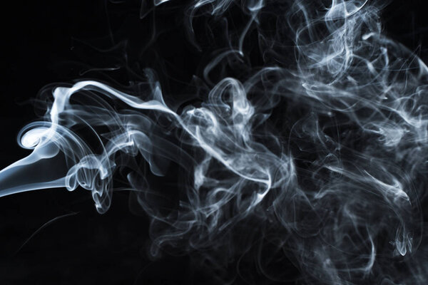 Background image of a wisp of smoke on a dark background. The texture of the flowing smoke. Frozen smoke on a dark background. Graphic resources dark backdrop. Texura of white clouds of fog. Curls of smoke frozen in motion.