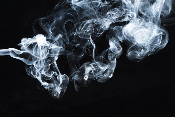 Background image of a wisp of smoke on a dark background. The texture of the flowing smoke. Frozen smoke on a dark background. Graphic resources dark backdrop. Texura of white clouds of fog. Curls of smoke frozen in motion.