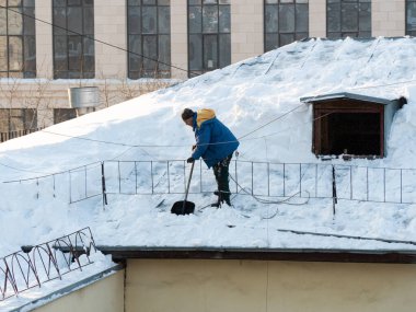 The hard work of removing snow from the trot of a building in the city. Snow removal with a shovel. Workers work at height. People are removing snow from the roof.