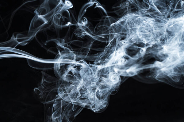 Background image of a wisp of smoke on a dark background. The texture of the flowing smoke. Frozen smoke on a dark background. Graphic resources dark backdrop. Texura of white clouds of fog. Curls of smoke frozen in motion.