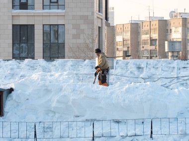 The hard work of removing snow from the trot of a building in the city. Snow removal with a shovel. Workers work at height. People are removing snow from the roof.