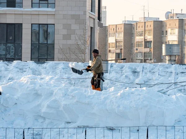The hard work of removing snow from the trot of a building in the city. Snow removal with a shovel. Workers work at height. People are removing snow from the roof.