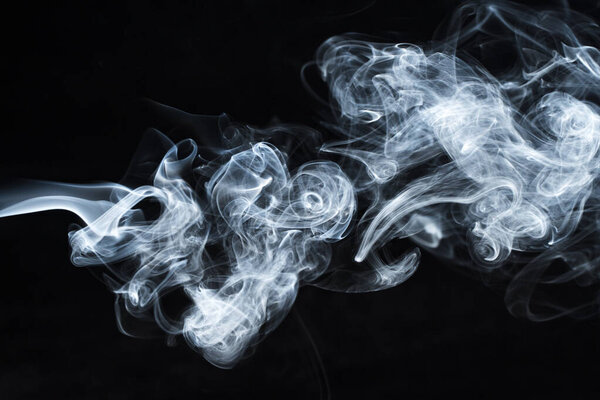 Background image of a wisp of smoke on a dark background. The texture of the flowing smoke. Frozen smoke on a dark background. Graphic resources dark backdrop. Texura of white clouds of fog. Curls of smoke frozen in motion.