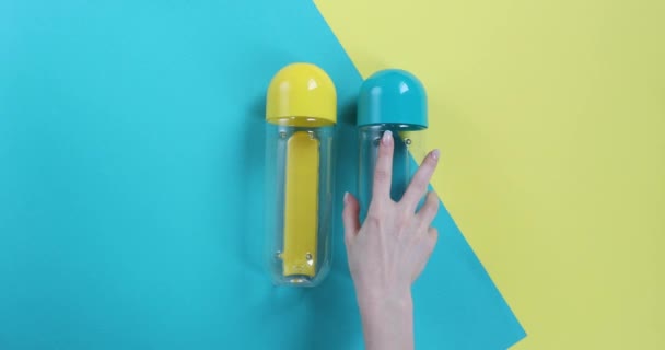 Garrafas Azuis Amarelas Jazem Sobre Fundo Azul Amarelo Uma Mão — Vídeo de Stock