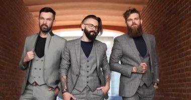 Gri takım elbiseli üç adam tuğla bir binaya karşı.