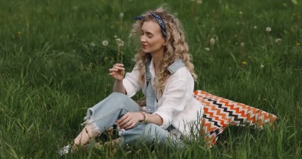 头发卷曲的女孩手拿鲜花坐在草地上 — 图库视频影像