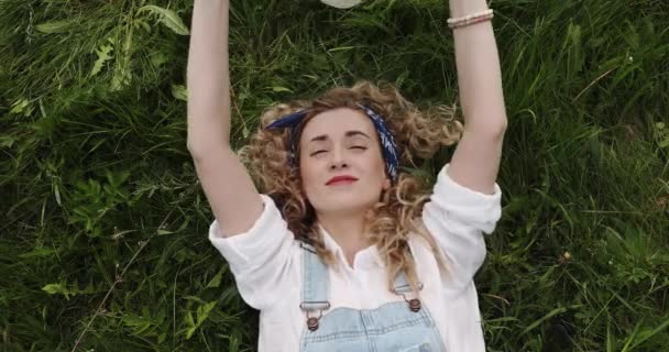 Жінка Кучерявим Волоссям Лежить Зеленій Траві Закриває Обличчя Капелюхом — стокове відео