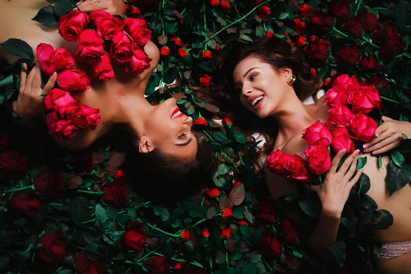İki esmer, kırmızı güllerle kaplı çiçeklerin üzerinde yatıyor. — Stok fotoğraf