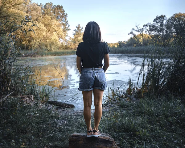 Arkadan kadın görüntüsü. Kadın ahşap bir buharın üzerinde durur ve suya bakar..