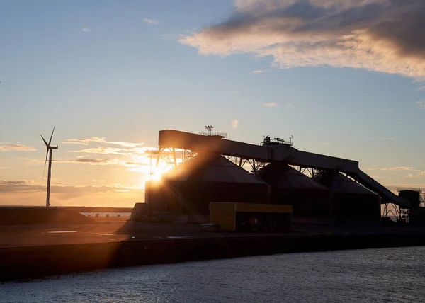 Kargo limanında gün batımı. Güneş büyük kargo deposunun arkasında. İskele. Peyzaj.