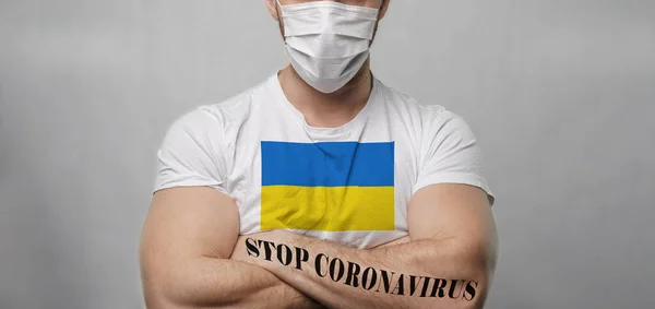 一位身穿白色T恤衫的年轻壮汉站在镜头前的浅色背景上 他的胳膊交叉在胸前 上面挂着乌克兰国旗的图案 手头上的纹身阻止考罗那威斯四 后续行动 — 图库照片
