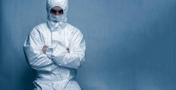 Un hombre vestido con un traje blanco protector y una máscara blanca cruzó sus brazos sobre su pecho. Tintado azul. Lugar para el texto —  Fotos de Stock