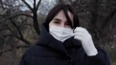 Siyah ceketli esmer bir kadın sokakta duruyor. Bir kadın koruyucu maske ve eldiven takıyor. Coronavirus. Yalıtım