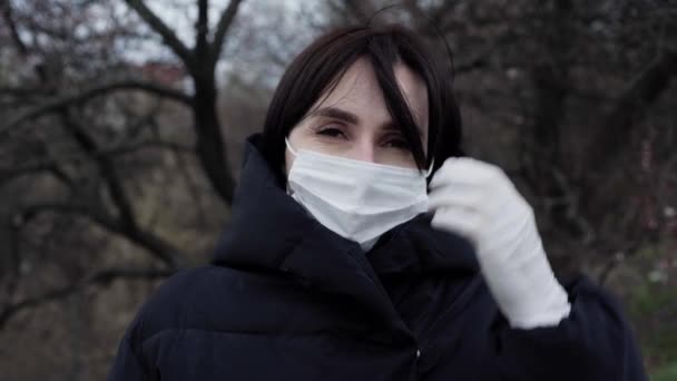 Una donna bruna in giacca nera si trova per strada. Una donna indossa una maschera protettiva e guanti. Coronavirus. Isolamento — Video Stock