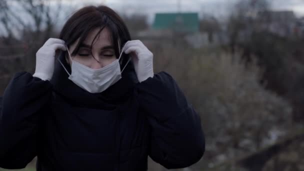 Μια μελαχρινή γυναίκα με μαύρο μπουφάν στέκεται στο δρόμο. Μια γυναίκα φοράει προστατευτική μάσκα και γάντια. Ιός του κερατοειδούς. Μόνωση — Αρχείο Βίντεο