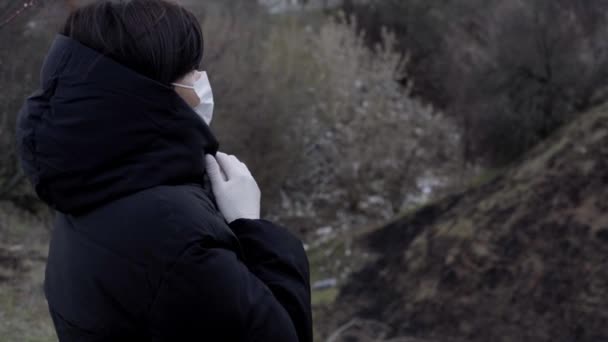 Una donna bruna in giacca nera si trova per strada. Una donna indossa una maschera protettiva e guanti. Coronavirus. Isolamento — Video Stock