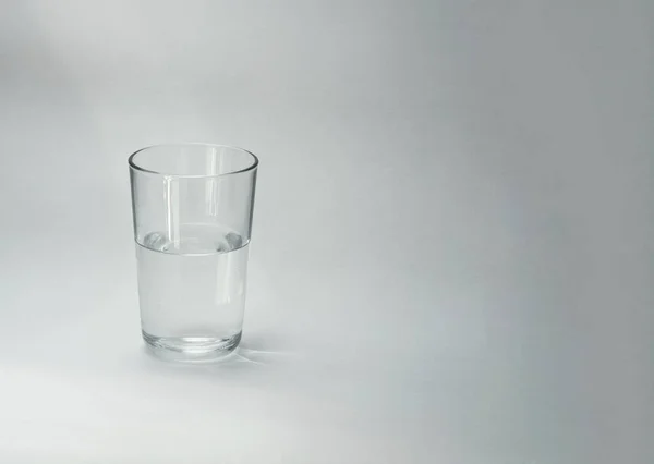 A glass cup half full of water stands on a light background. Close-up. Copy space