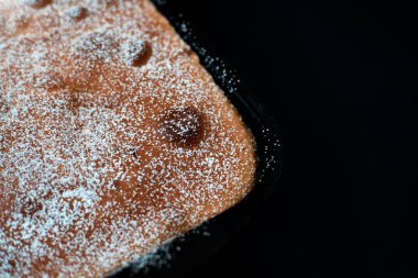 Taze pişmiş bir elmalı turta metal bir fırın tepsisinde yatıyor. Pasta pudra şekerle serpilmiş. Siyah arka plan. Yakın plan. Boşluğu kopyala