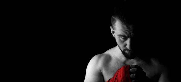 Banner image of a mans fighter with a beard and red bandages on his hands. Head down, look from beneath the forehead. Black white image with red. Place for text. Black background