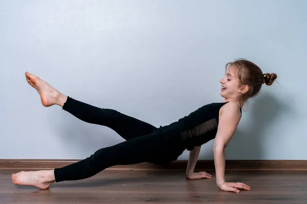 Açık tenli, sarışın bir kız karantina sırasında evde spor yapıyor. Siyah eğitim üniformalı atletik kız. Spor egzersizleri evde..