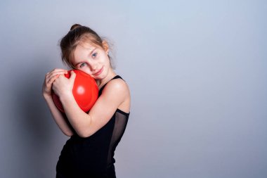 Siyah spor tişörtlü beyaz tenli bir kız kırmızı bir jimnastik topu tutuyor ve göğsüne bastırıyor. Spor aşkı. Metin için yer.