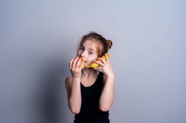 Siyah kazaklı beyaz tenli bir kız elinde bir elma ve bir muz tutuyor. Meyvenin faydaları. Metin için sağlıklı yeme yeri.