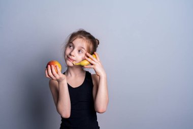 Siyah kazaklı beyaz tenli bir kız elinde bir elma ve bir muz tutuyor. Meyvenin faydaları. Metin için sağlıklı yeme yeri.