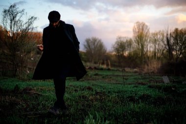 Koyu saçlı, sakallı, doğada sigara içen bir adamın sanatsal portresi. Koyu renk elbiseler, kafasında bir şapka. Film için film işleme.