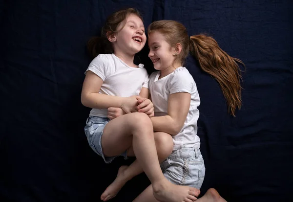 Девушки Лежат Синем Фоне Весело Смеются Щекоча Друг Друга Дружба — стоковое фото