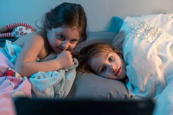 两个小妹妹晚上躺在床上 看着平板电脑上的卡通片 电影拍摄 孩子们的夜晚假期 睡前故事 图库图片