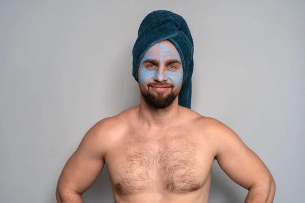 一个留着胡子 头上戴着蓝色毛巾 脸上戴着化妆品的男人 男人的美容程序 男子的皮肤护理 免版税图库照片