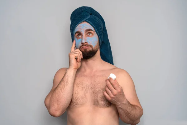 一个留着胡子 头上戴着蓝色毛巾 脸上戴着化妆品的男人 男人的美容程序 男子的皮肤护理 免版税图库图片