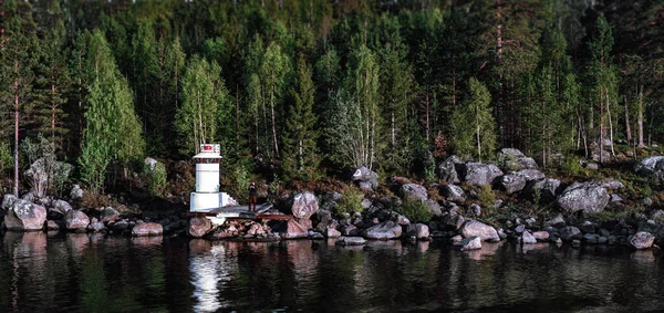 瑞典美丽的自然。一个有石头和树木的岛屿一个男人站在码头上，用电话拍照. 图库照片