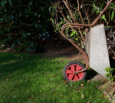 Garden wheelbarrow with red wheel standing on end beside grass lawn clipart