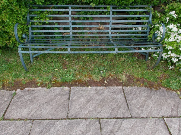 Зеленая металлическая скамейка на грубой траве с тротуарной плиткой на переднем плане — стоковое фото