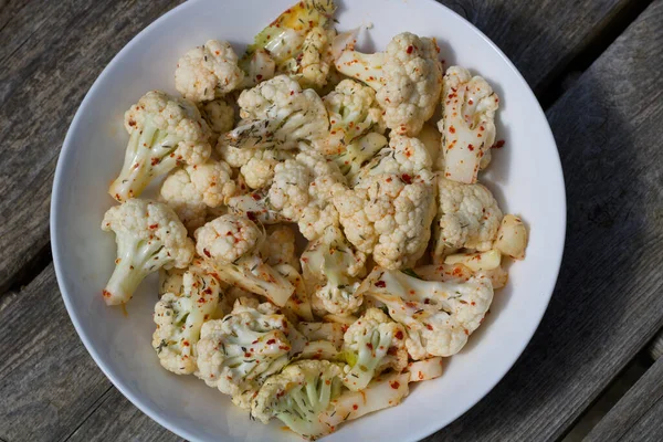 Bir kase baharatlı karnabahar ve tabakta kırmızı biber.