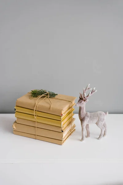 Books in craft covers in a stack, tied with a scourge, next to it is a Christmas deer figurine on a gray background