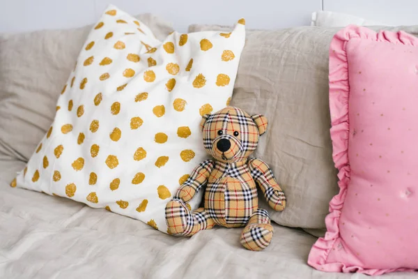Soft toy plaid bear among pillows on the bed