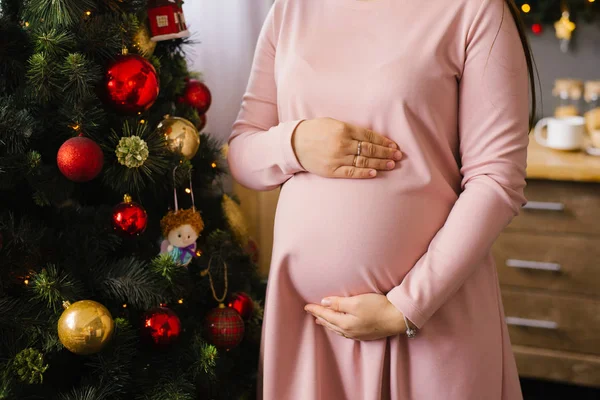 Kvinna Håller Händerna Sin Gravida Mage Bakgrunden Julgran Ljus — Stockfoto